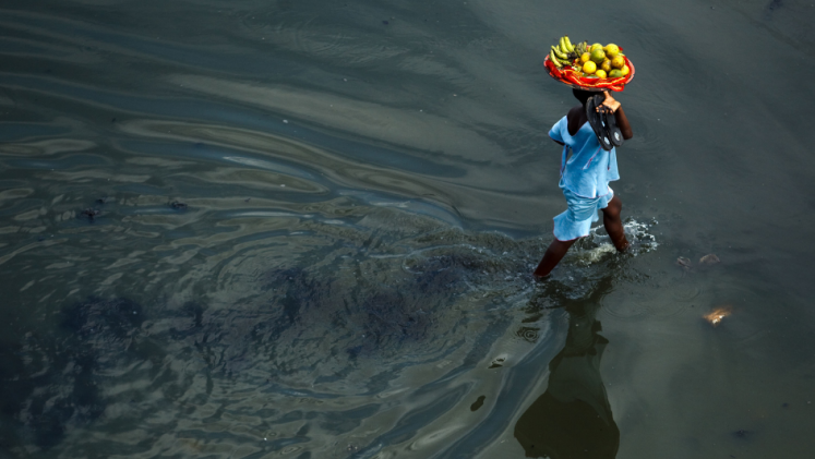 A person walking in water with a basket of fruits