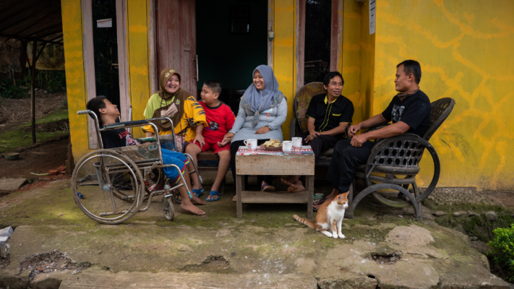 A family sitting outside and smiling, with one boy in a wheelchair